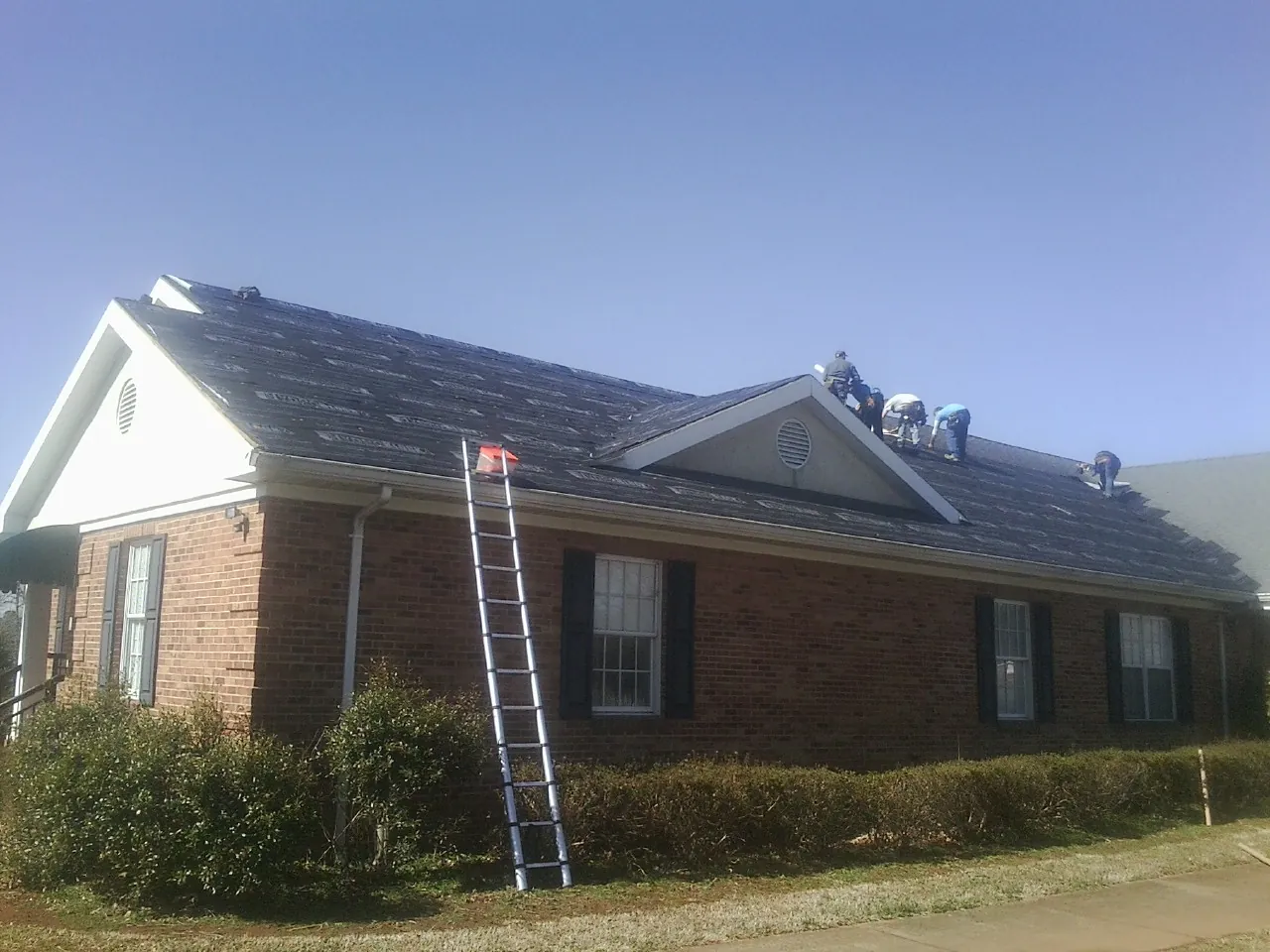 Crew tearing shingles off a brick ranch roof with a ladder set — Metal Roof Repair work by our crew in Athens