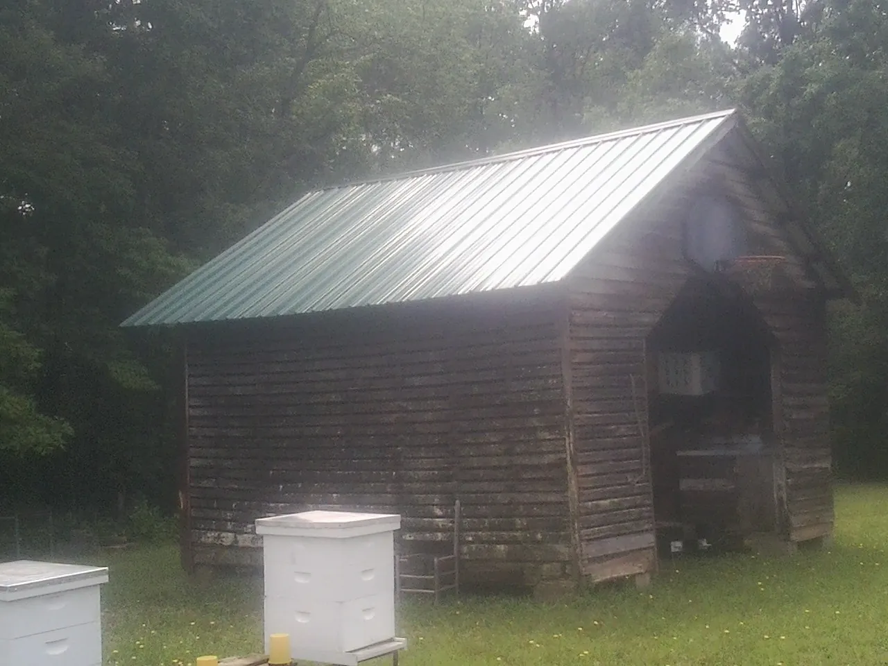 Green metal roof on a weathered barn beside stacked beehives in Athens