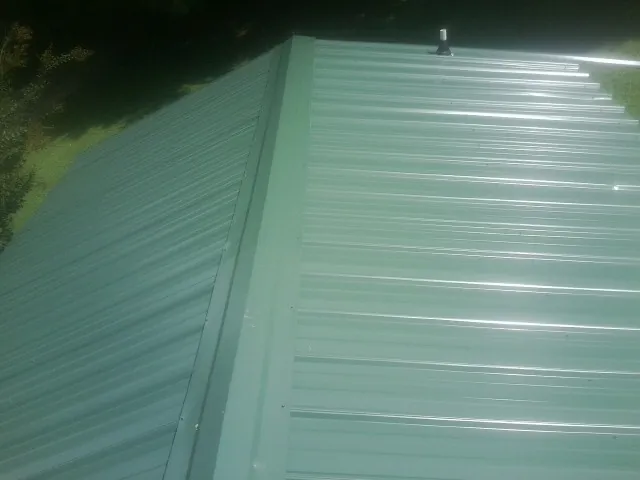 New green metal panels meeting at the ridge of a roof — Flat Roof Repair work by our crew in Athens